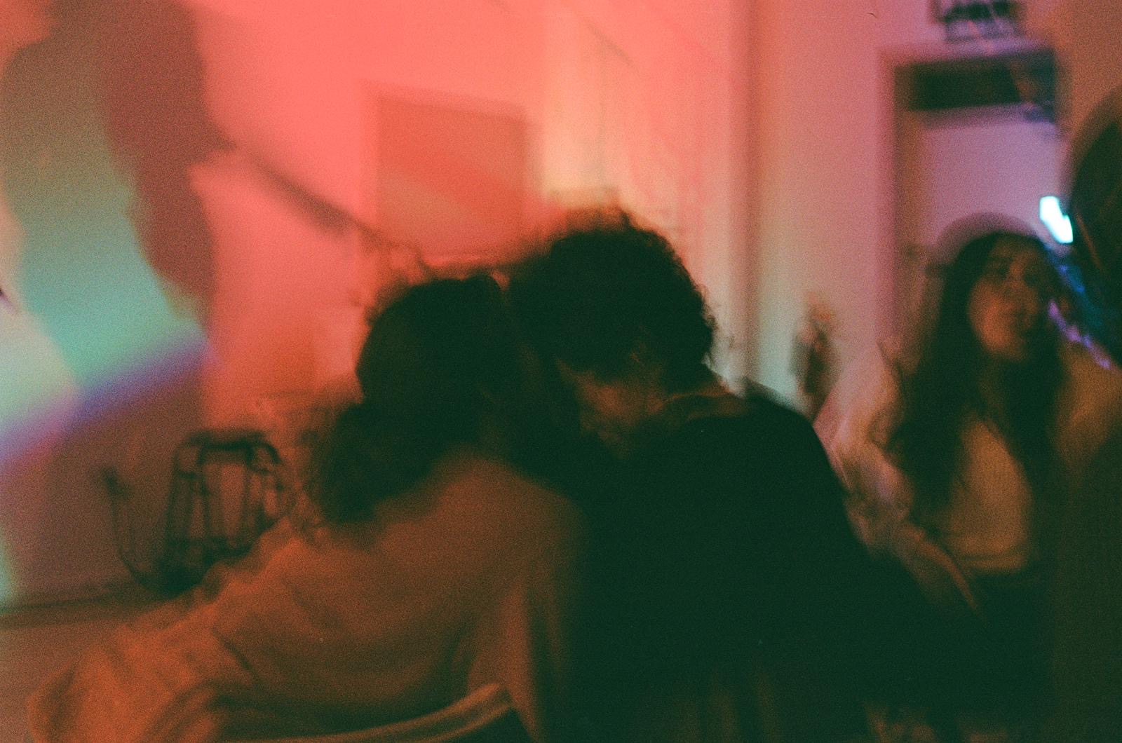 a photo of Amelie whispering to (?) kissing (?) sharing something wonderful with Soph, obscured by Sean's blurry camera, they are a haze of burnt orange and cyan